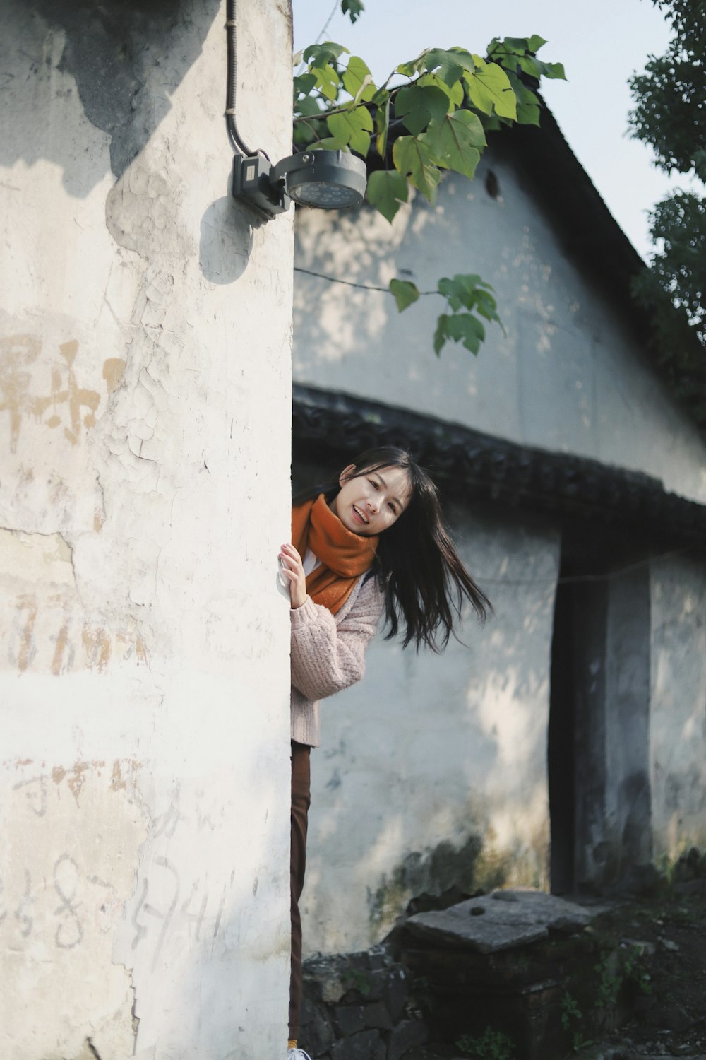 smiling woman hiding behind gray wall during daytime