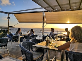 Guests enjoying a sunset dinner on a wooden deck by the sea.