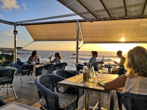 Guests enjoying a sunset dinner on a wooden deck by the sea.