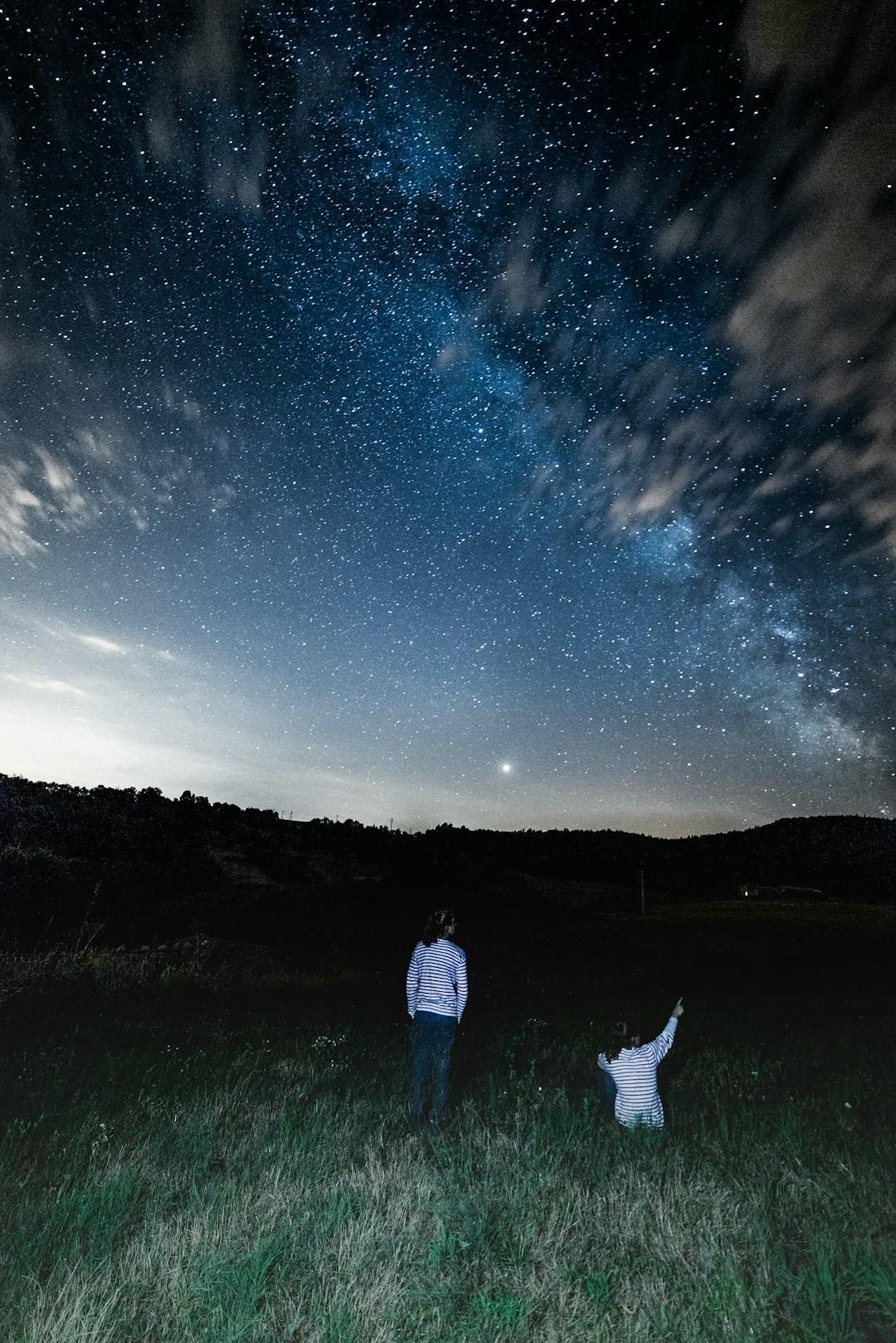 2 people in white shirts in field watching star formations in night sky