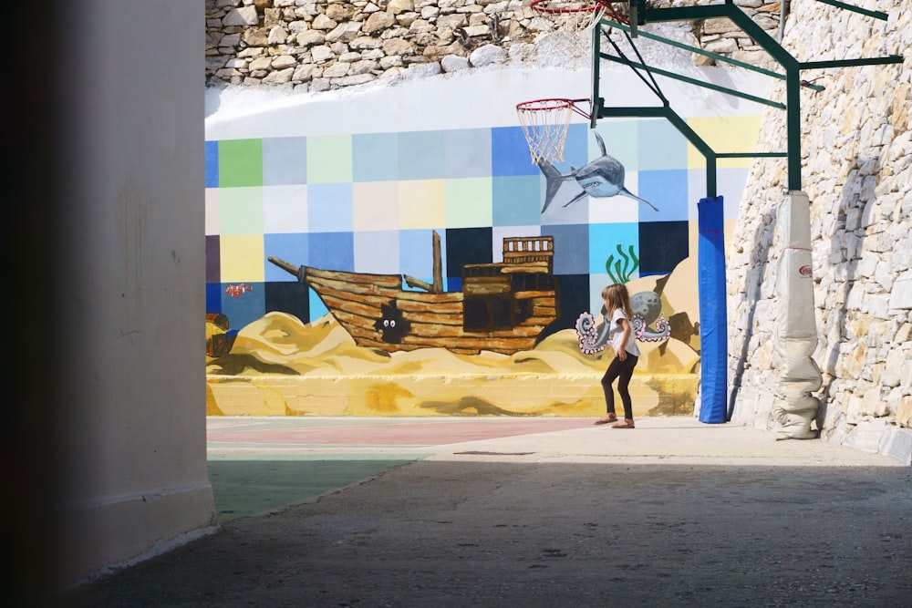 girl standing near basketball hoop and boat mural