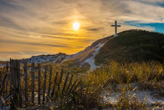 white cross on grass covered hilltop during sunrise