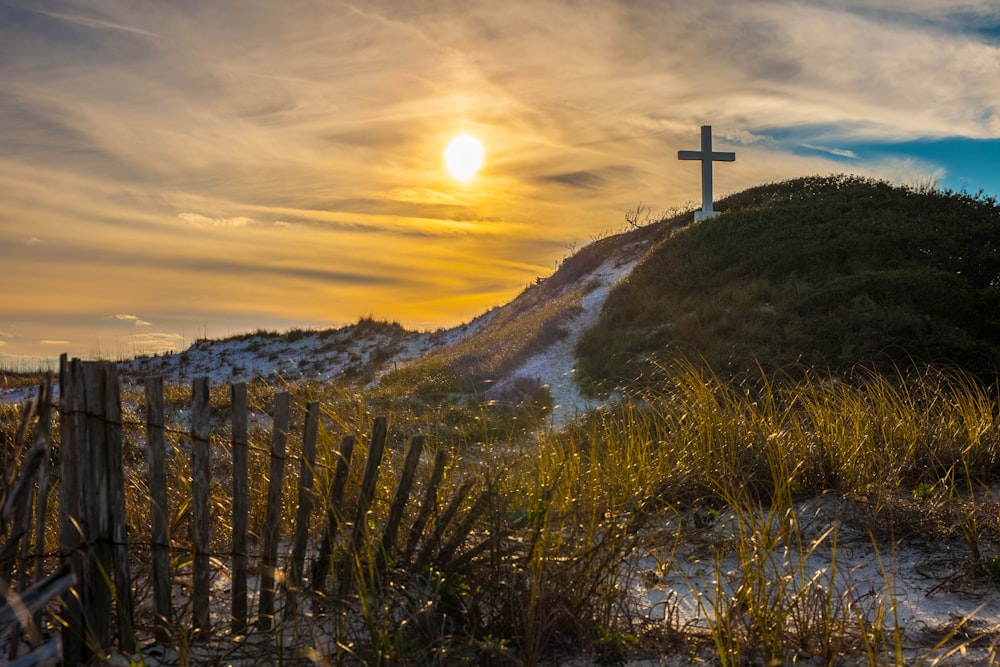 white cross on grass covered hilltop during sunrise