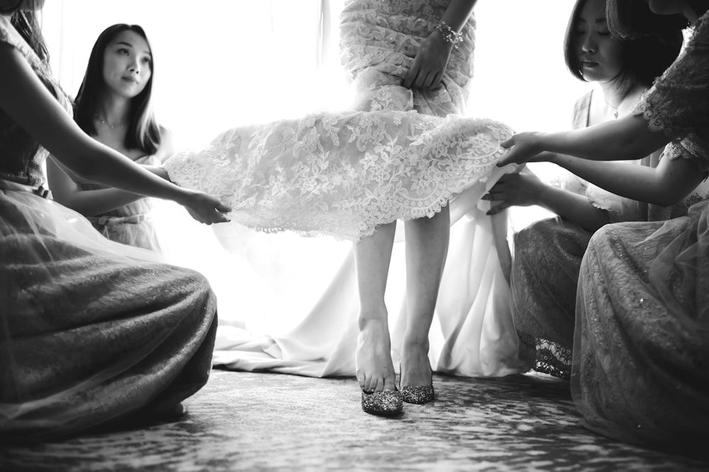 4 women holds hem of another woman's white dress