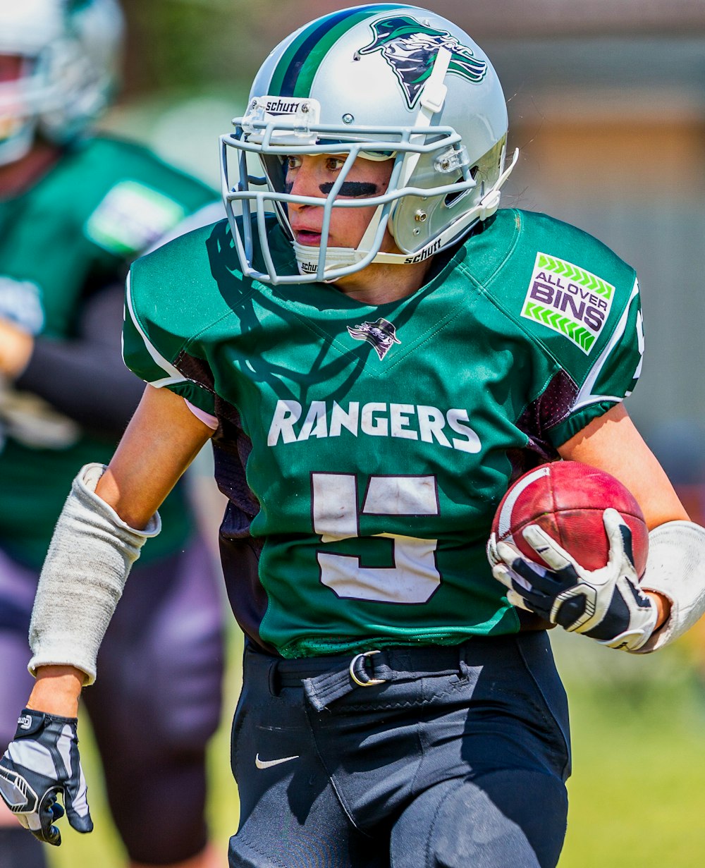 man in green Rangers football uniform holds ball