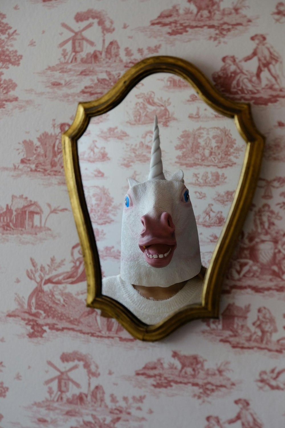 person with white unicorn mask stands in front of wall mirror