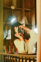 A woman smiling while holding a camera in a well-decorated space.