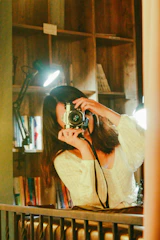 Woman photographing clothes on a wooden hanger in a cozy, softly lit room.