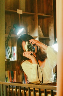 A woman smiling while holding a camera in a well-decorated space.