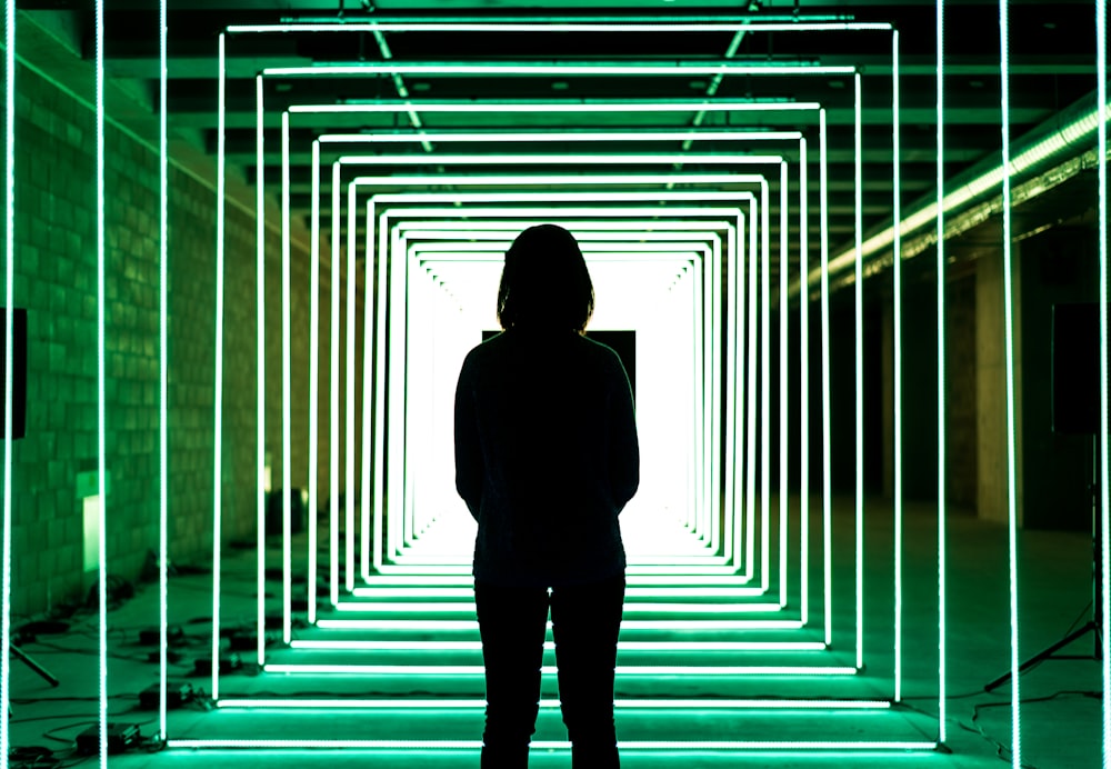 silhouette of woman standing in middle of green neon lighted cage