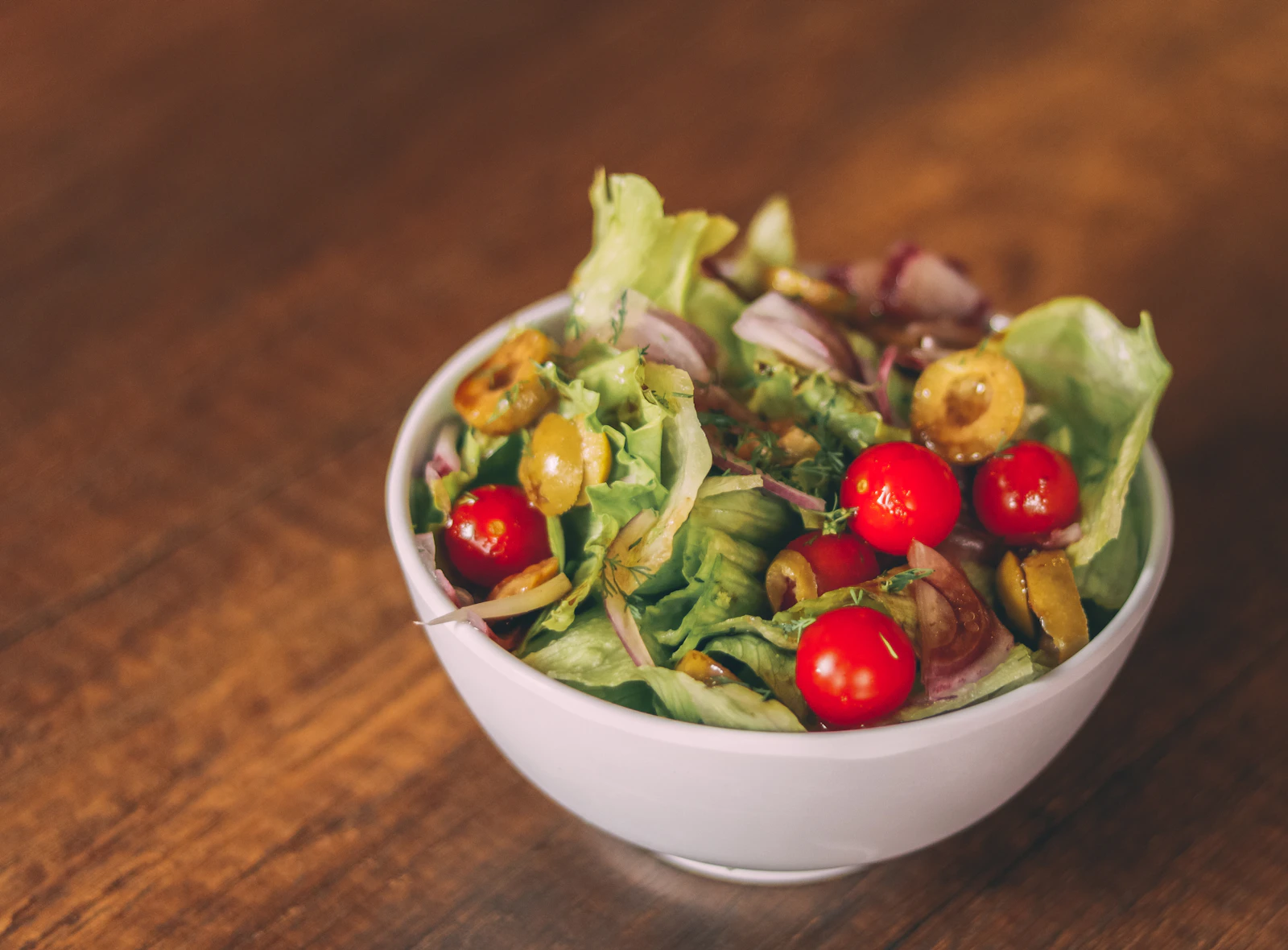 A bowl of green salad with cherry tomatoes and olives