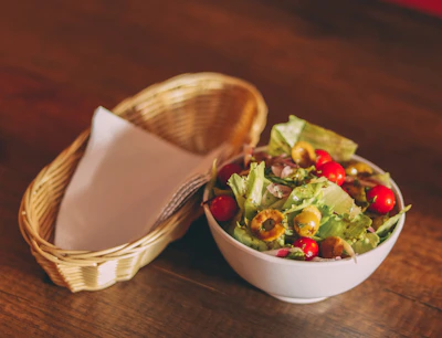 A rustic ceramic bowl filled with fresh salad on a wooden table.