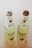 Two green bottles, labeled as mojito, are placed side by side. The bottles have a simple design with a citrus slice sticker and capped with metallic lids. The background is light and neutral, enhancing the freshness look of the bottles.