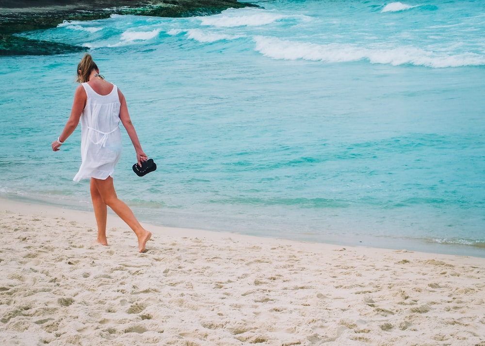 woman in white dress walks on white sand beach
