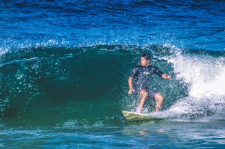 A surfer rides a powerful wave in the ocean, demonstrating balance and skill on a surfboard. Water sprays around him, creating a dynamic and energetic scene.