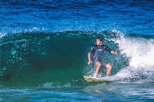 A surfer rides a powerful wave in the ocean, demonstrating balance and skill on a surfboard. Water sprays around him, creating a dynamic and energetic scene.