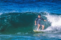 A surfer rides a powerful wave in the ocean, demonstrating balance and skill on a surfboard. Water sprays around him, creating a dynamic and energetic scene.