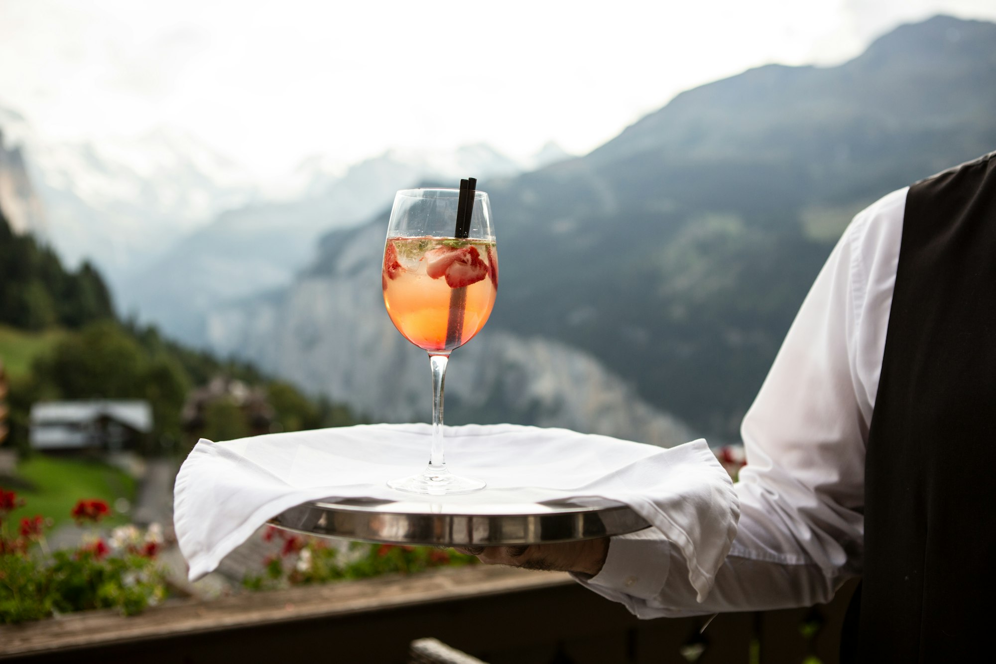 A waiter serving a glass of cocktail with a mountain view in the background