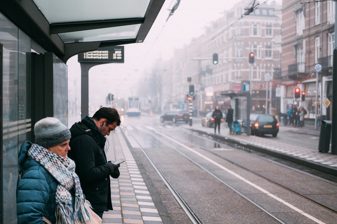 man and woman standing on sidewalk using smartphone during daytime