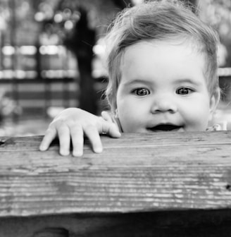 greyscale photo of baby on wooden bench