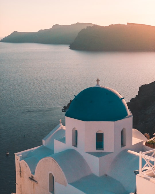 white and teal painted building near on seashore in Oia Greece