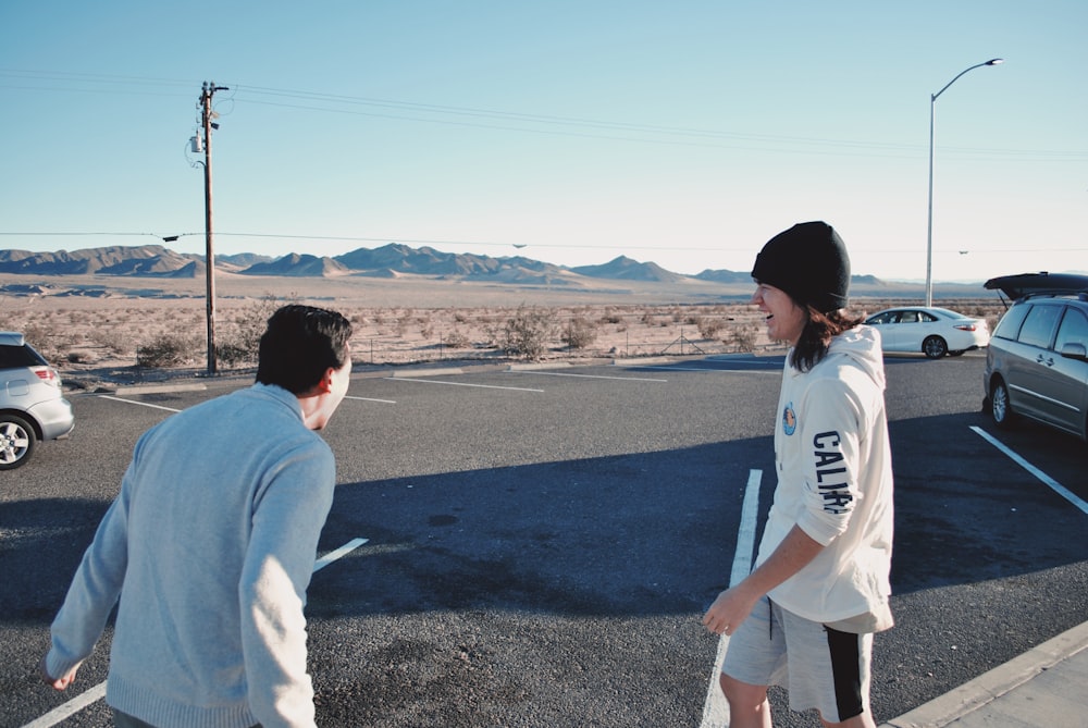 man wearing white hoodie standing beside man wearing gray sweatshirt on road near vehicles during daytime