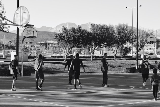 A diverse group of people playing basketball together outdoors, smiling and supporting each other.