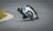 A motorcyclist is leaning sharply into a curve on a racetrack. The rider is wearing full protective gear including a helmet and a black suit with neon yellow accents. The motorcycle is white and appears to be moving at high speed. The track is wide and empty with some grass visible to the side.