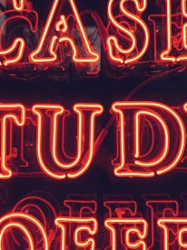 Bright red neon letters forming part of a larger sign that appears to possibly spell out 'CASE STUDY.' The background is dark, making the neon letters stand out prominently.