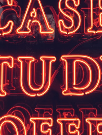 Bright red neon letters forming part of a larger sign that appears to possibly spell out 'CASE STUDY.' The background is dark, making the neon letters stand out prominently.