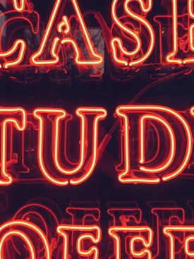 Bright red neon letters forming part of a larger sign that appears to possibly spell out 'CASE STUDY.' The background is dark, making the neon letters stand out prominently.