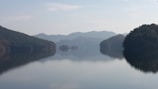 A serene view of Waduk Jatiluhur with calm water reflecting the green hills under a clear sky