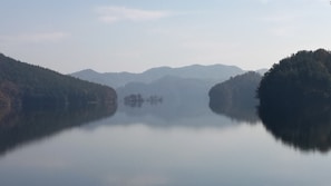 A serene view of Waduk Jatiluhur with calm water reflecting the green hills under a clear sky