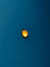 A close-up of a deep gold lighting fixture casting a warm glow against a matte blue wall.