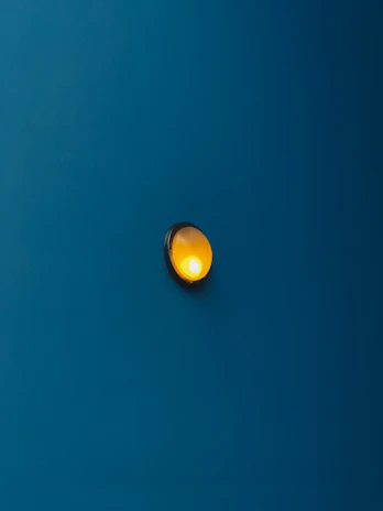 A close-up of a deep gold lighting fixture casting a warm glow against a matte blue wall.