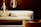 A cozy and modern living space featuring a light-colored sofa with a matching pillow in front of a dark brick wall. Two large, stylish pendant lights with visible filaments hang from the ceiling, casting a warm glow. An armchair in complementary tones is situated nearby.