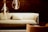A cozy and modern living space featuring a light-colored sofa with a matching pillow in front of a dark brick wall. Two large, stylish pendant lights with visible filaments hang from the ceiling, casting a warm glow. An armchair in complementary tones is situated nearby.