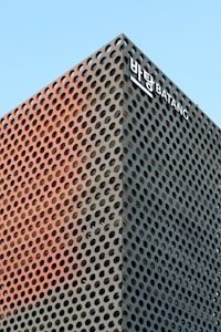A modern architectural structure with a perforated metallic facade, featuring circular patterns across its surface. The building is set against a clear blue sky and has a sign with text in both Korean and English near the top.