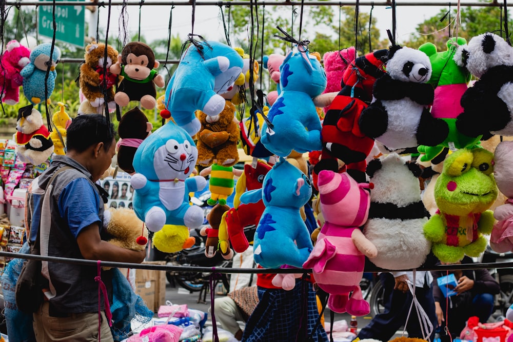 homme en polo bleu debout devant la couleur assortie de l’affichage de lot de jouets en peluche