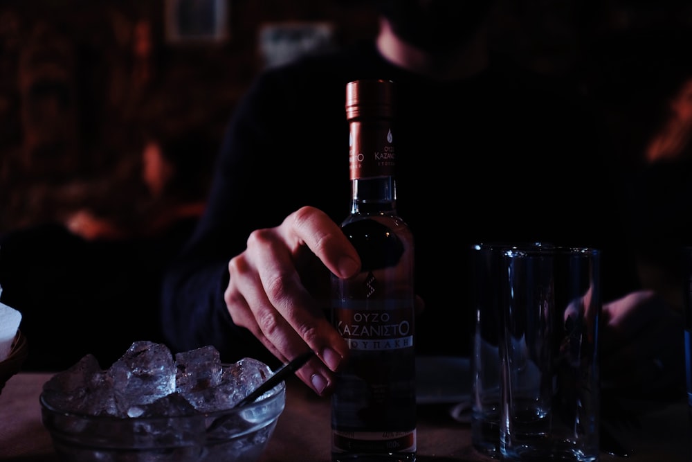 man in black shirt holding a bottle of drink at bar