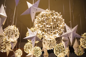 Hanging decorations feature illuminated wire spheres intertwined with string lights and paper stars adorned with small stars, creating a festive and whimsical atmosphere.