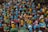 A large group of colorful, handcrafted clay figurines representing women with various poses and expressions. The figurines feature bright blue and yellow faces, each adorned with unique hairstyles and traditional attire in shades of red, green, and blue. They are closely packed together, creating a vibrant and diverse display of artistic craftsmanship.
