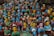 A large group of colorful, handcrafted clay figurines representing women with various poses and expressions. The figurines feature bright blue and yellow faces, each adorned with unique hairstyles and traditional attire in shades of red, green, and blue. They are closely packed together, creating a vibrant and diverse display of artistic craftsmanship.