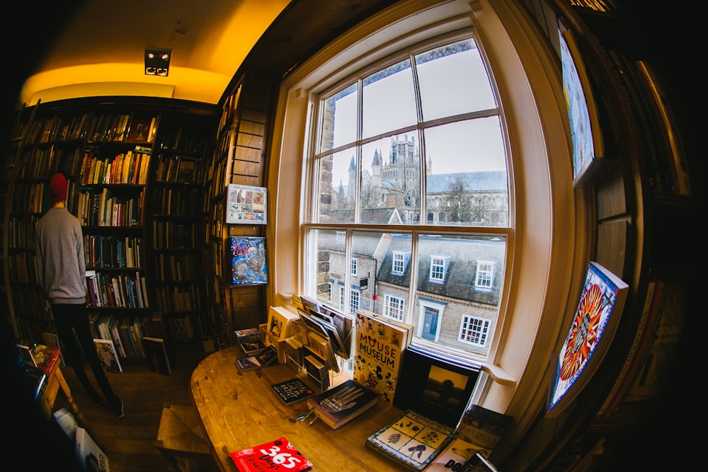 man in grey jacket standing in front of shelves with books in fish eye lens photography