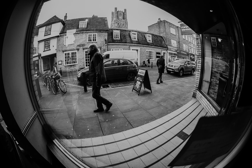 grayscale photo of person walking near car