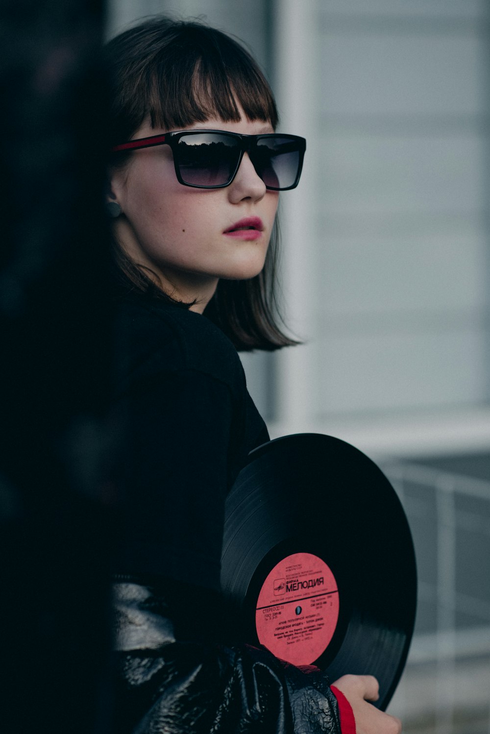 woman in black sunglasses and jacket holding vinyl record
