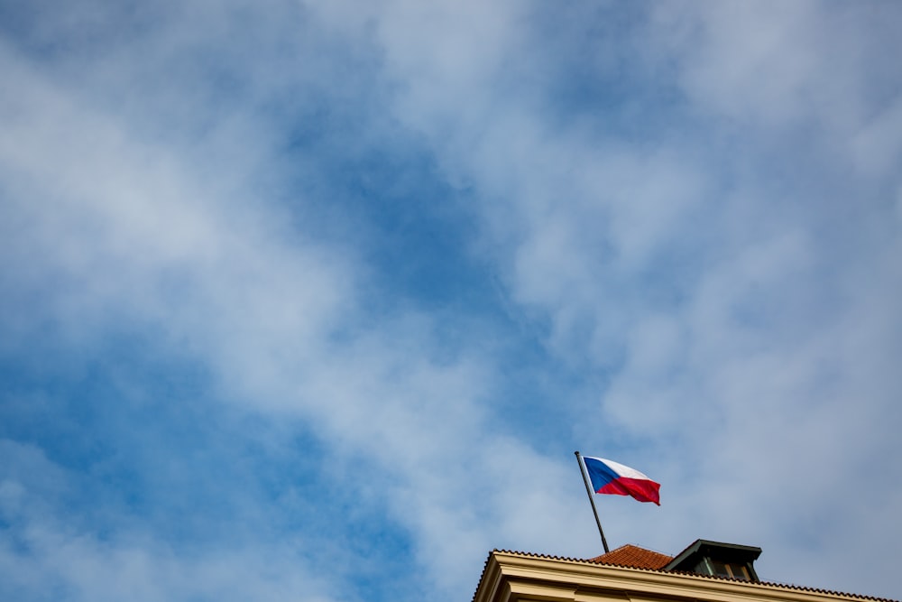 white, blue, and red flag hoisted atop brown building under cloudy sky