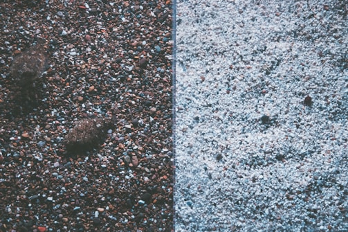 The image displays a split view of two different textures of gravel or pebbles. The left side features darker, multicolored stones with a few larger rocks, creating a rich, earthy texture. The right side contrasts with lighter-colored, predominantly white pebbles, offering a more uniform and subtle appearance.