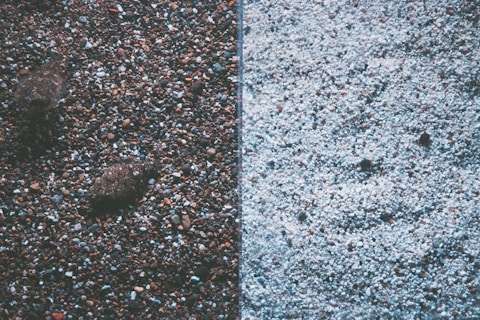 The image displays a split view of two different textures of gravel or pebbles. The left side features darker, multicolored stones with a few larger rocks, creating a rich, earthy texture. The right side contrasts with lighter-colored, predominantly white pebbles, offering a more uniform and subtle appearance.