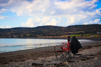 A rugged leather jacket draped over a weathered wooden chair on a rocky coastline at sunset.